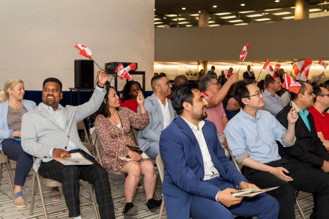 New Canadians celebrating by waving small Canadian flags in the air.